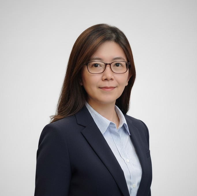 A professional woman with long, straight hair and glasses, wearing a dark blazer over a light blue shirt. She is positioned against a neutral gray background.