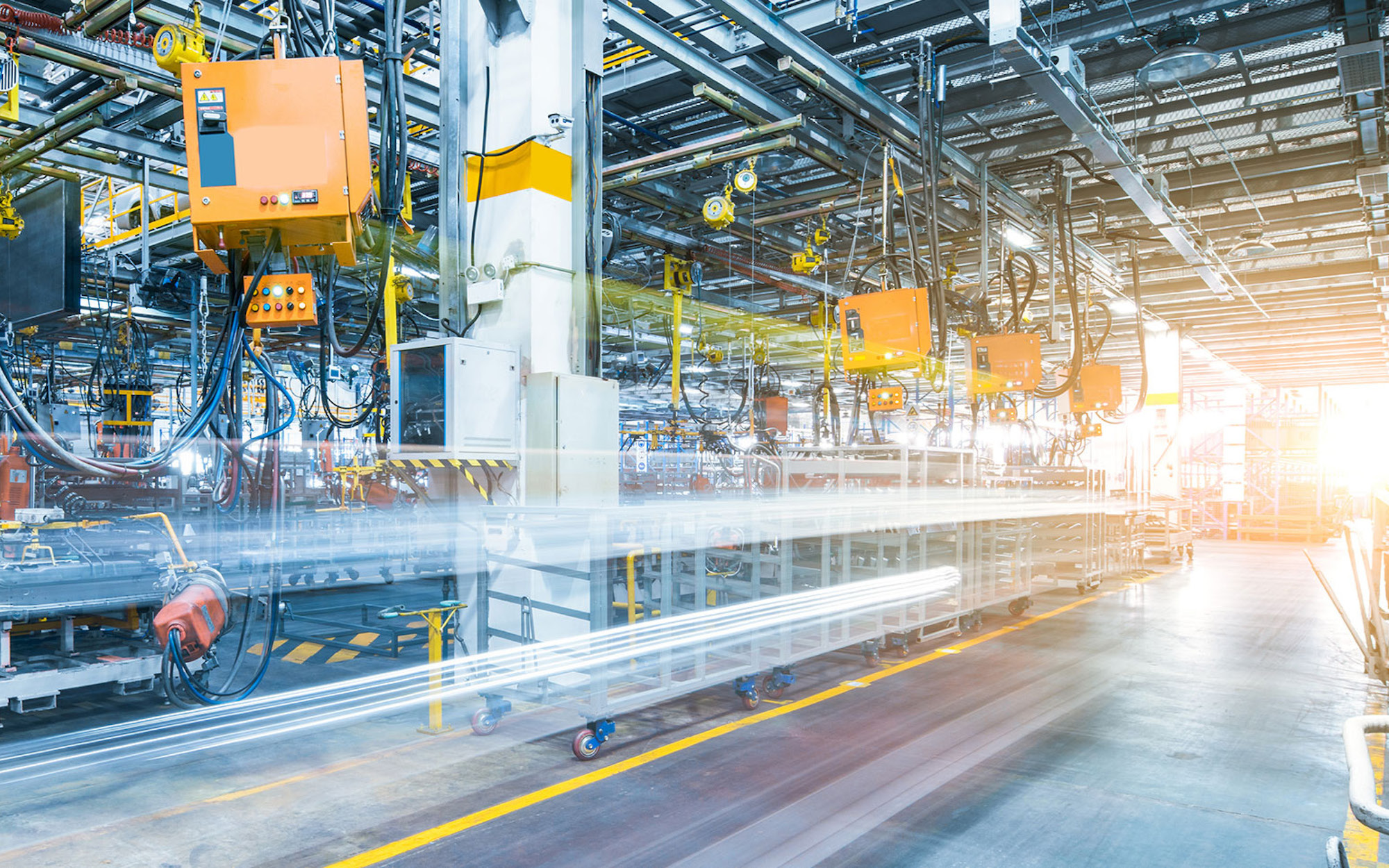 A modern manufacturing facility with industrial machinery and robotic arms. The environment is well-lit, showcasing a busy assembly line with various tools and equipment along the aisles.