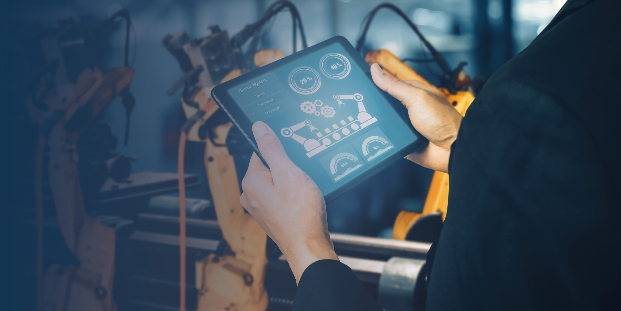 A person in a suit holds a tablet displaying a digital interface with gears and gauges, while robotic arms are visible in the background, suggesting a manufacturing or automation setting.