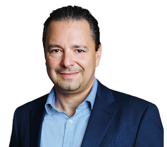 A man with dark hair, wearing a navy blue suit and a light blue shirt, smiles confidently.