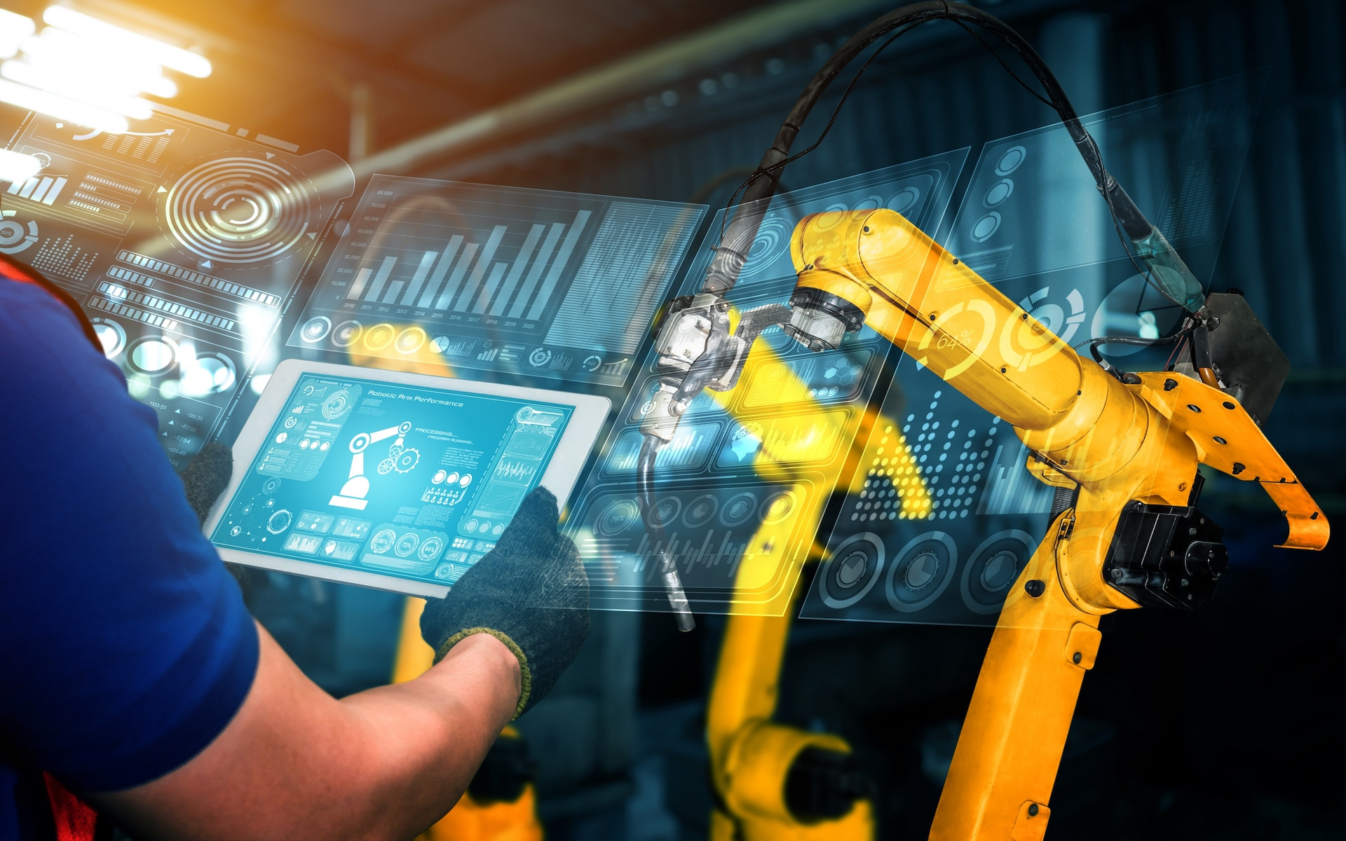 A worker wearing gloves operates a tablet, displaying data and graphs, while interacting with robotic arms in an industrial setting. The background features multiple yellow robotic arms, highlighting a modern automation environment.