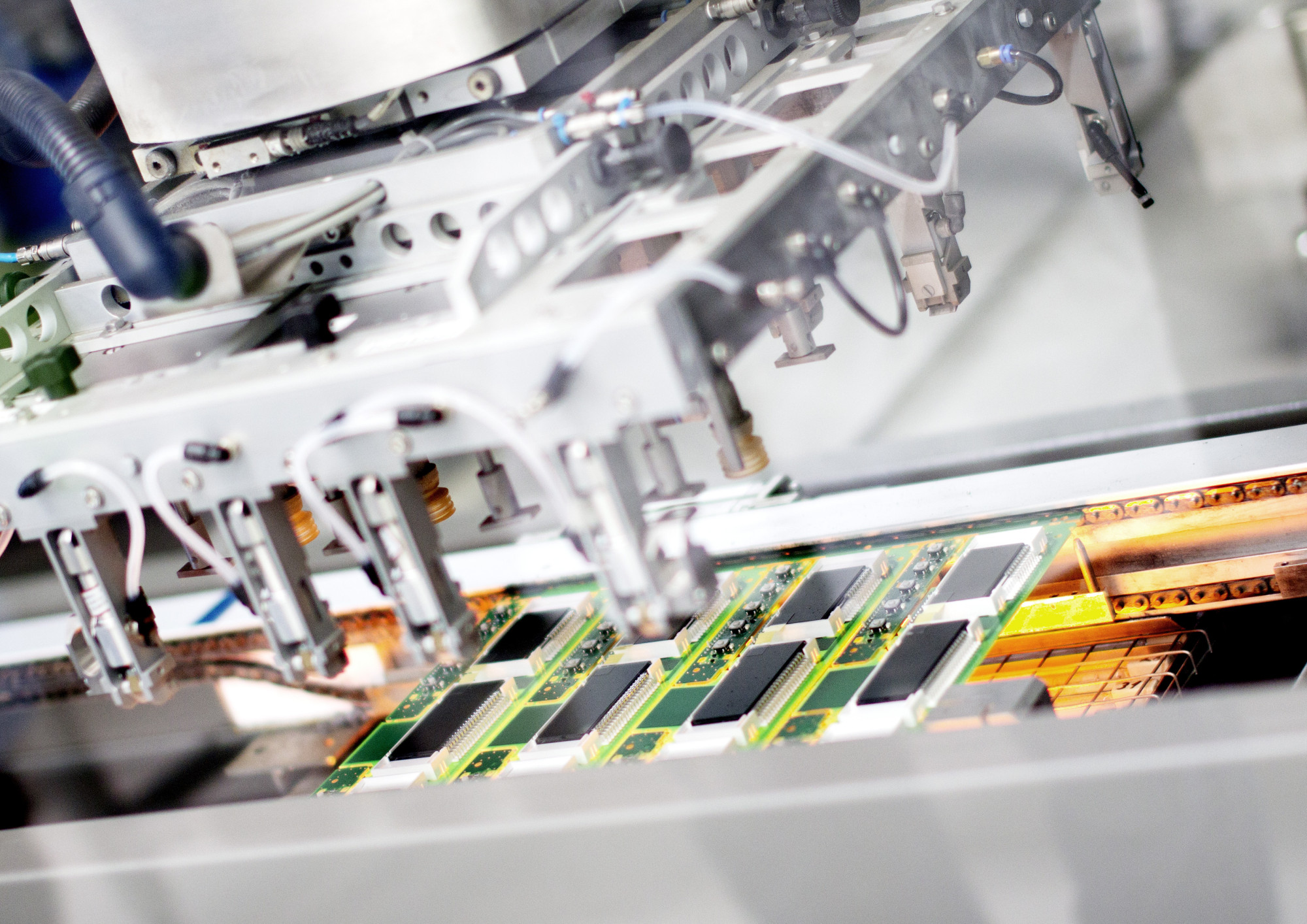 A close-up view of a robotic assembly machine working on printed circuit boards with multiple arms positioned accurately above the boards.