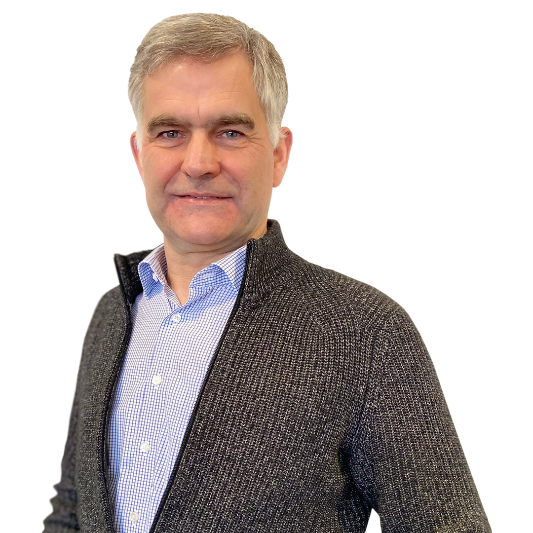 A smiling middle-aged man with short gray hair wearing a dark sweater over a light blue checkered shirt. He stands confidently, looking directly at the camera.
