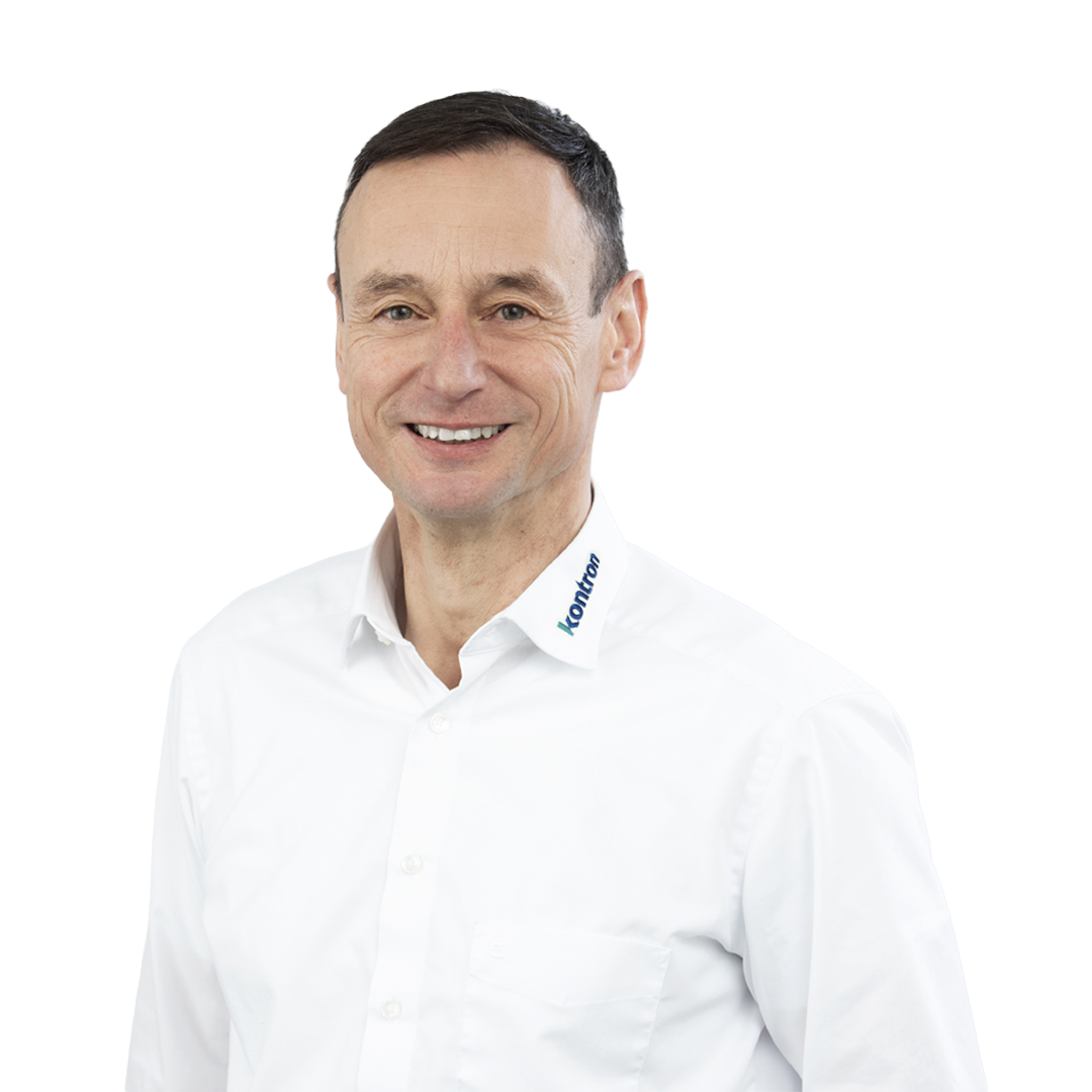 A smiling man wearing a white shirt with a blue logo on the collar. He has short dark hair and is standing against a white background.