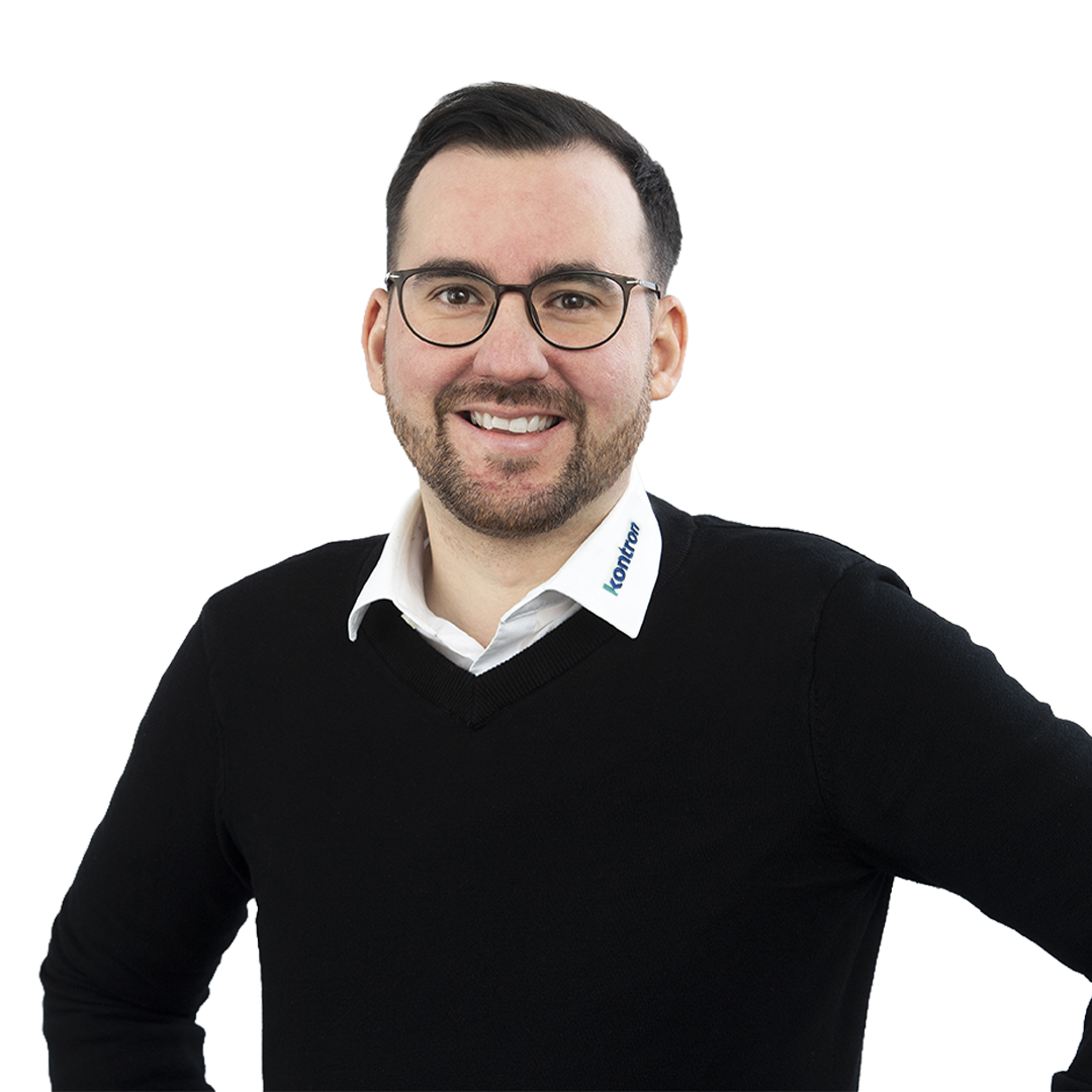 Smiling man with glasses, wearing a black sweater over a collared shirt, poses confidently with one hand on his hip. A logo is visible on the collar.
