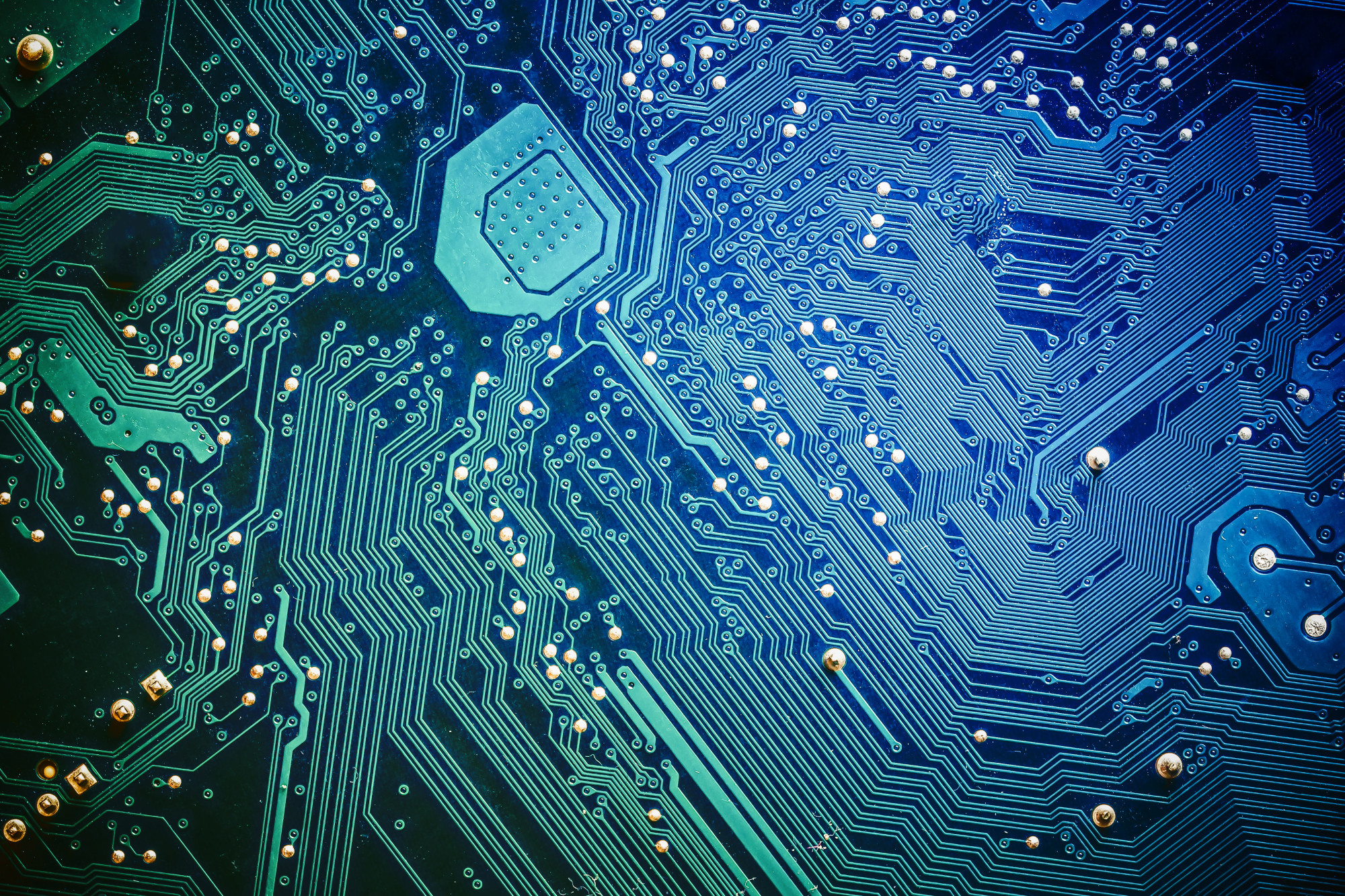 Close-up of a blue circuit board with intricate patterns of lines and circuits, featuring metallic components and small soldering points.