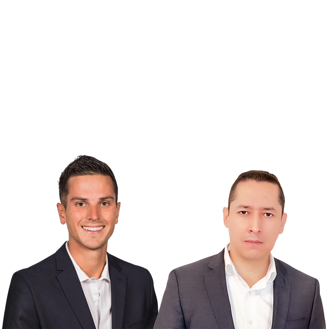 Two men in business attire stand side by side, smiling. One is wearing a dark blazer over a white shirt, while the other has a lighter outfit, also in a suit. The background is plain and white.